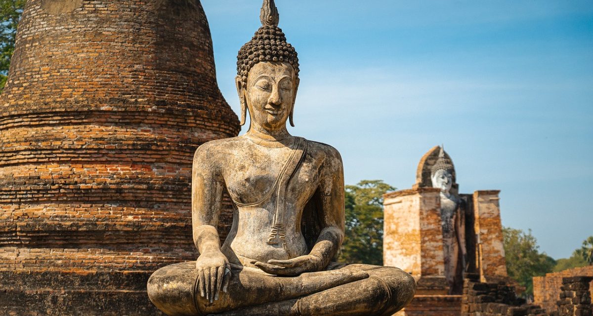Statue de Bouddha assis devant un ancien stupa en briques